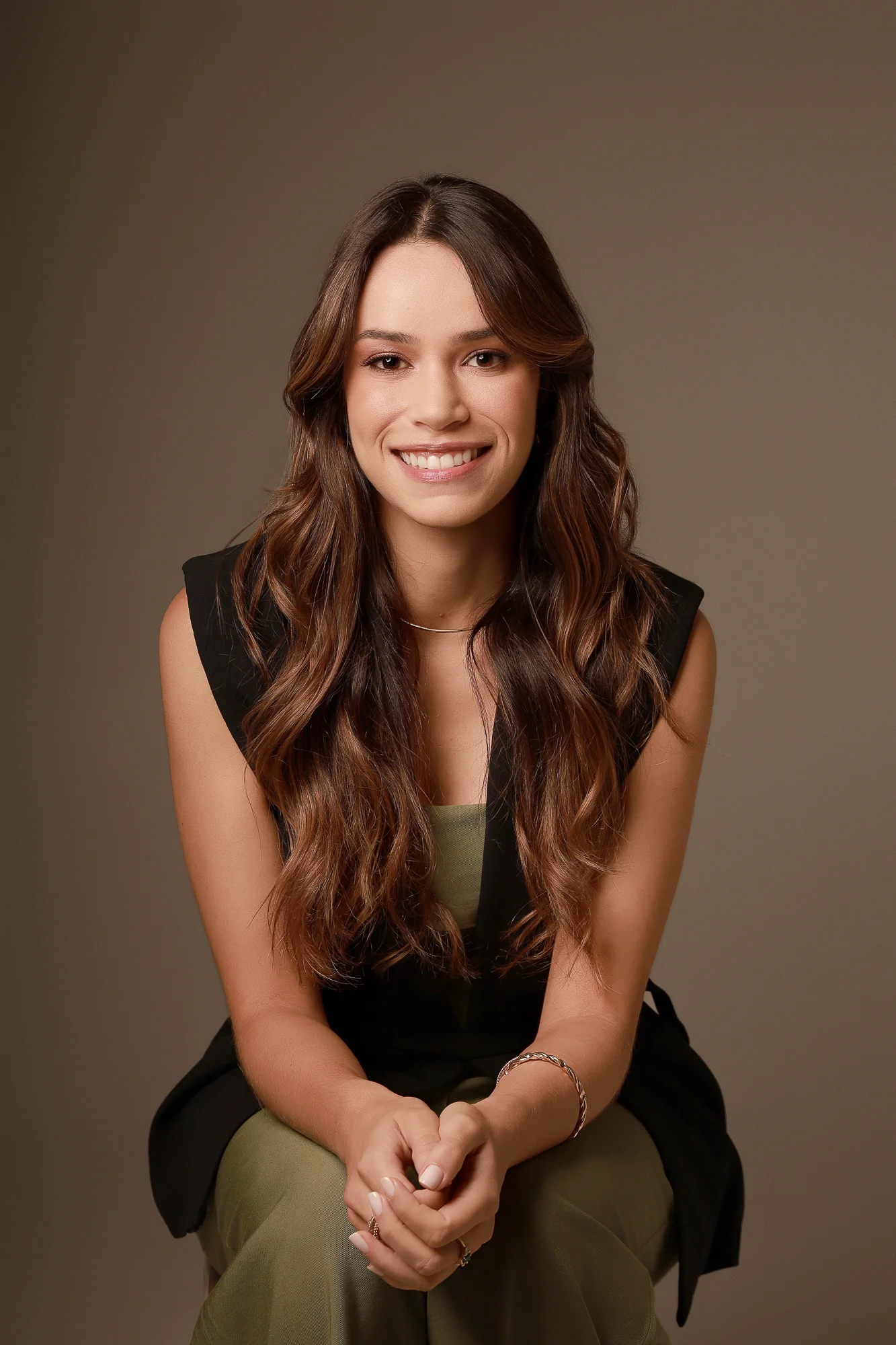 Dra. Mariana Sathler sentada, sorrindo, usando colete preto e traje verde.